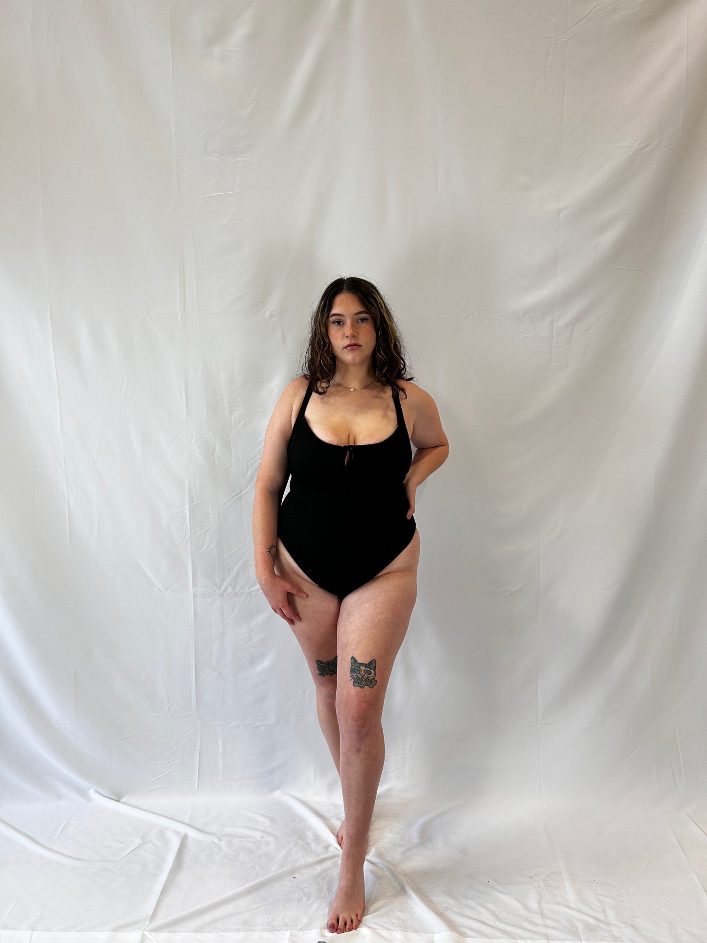 Model wears the black one piece. Model wears the milkmaid style tie front crinkle fabric one piece. Black one piece is high cut and cheeky.