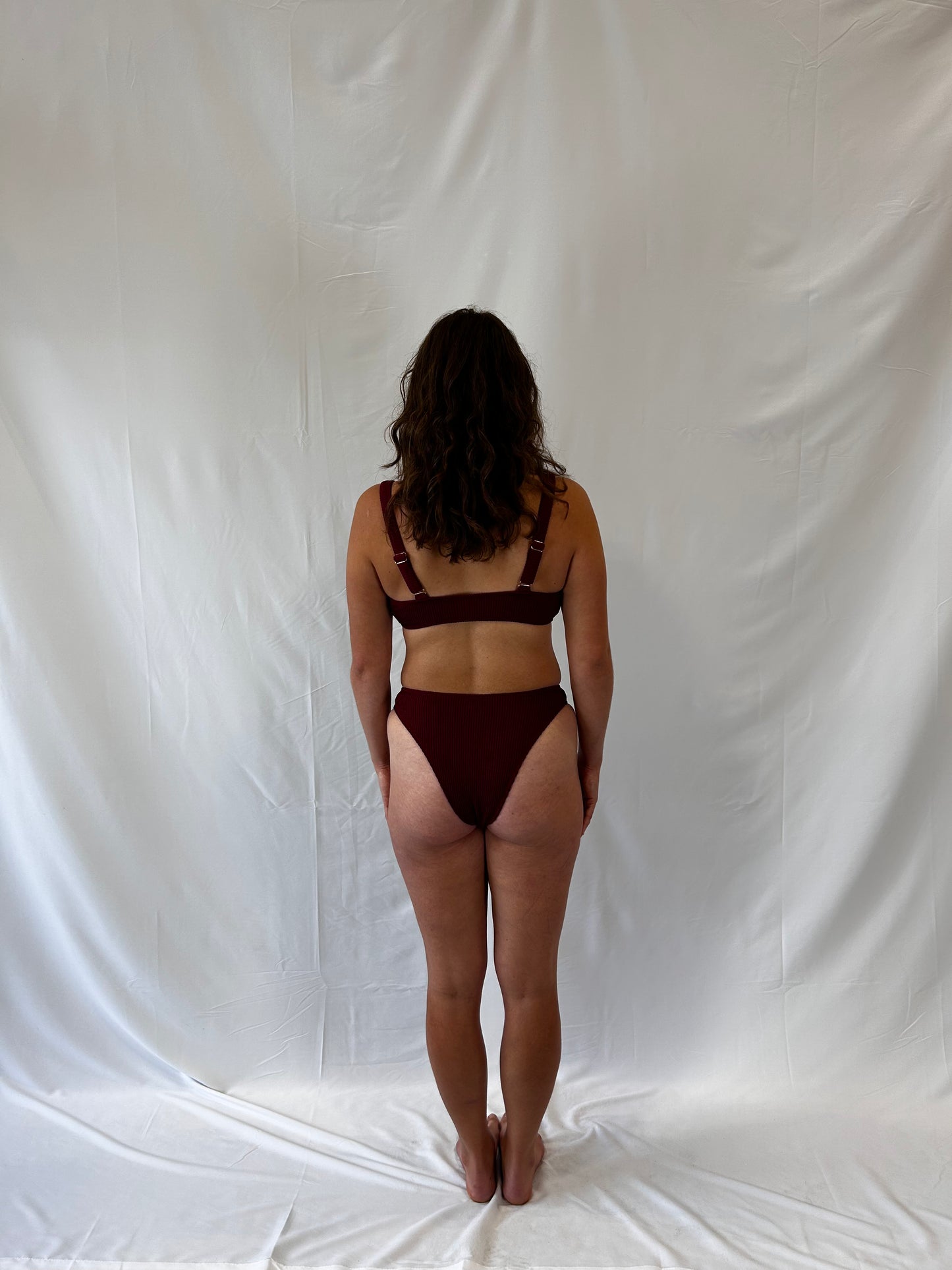 Bikini top is the milkmaid style tie front crinkle fabric. Bikini bottom is the high rise cheeky textured crinkle fabric. Burgundy two piece bikini from the back.