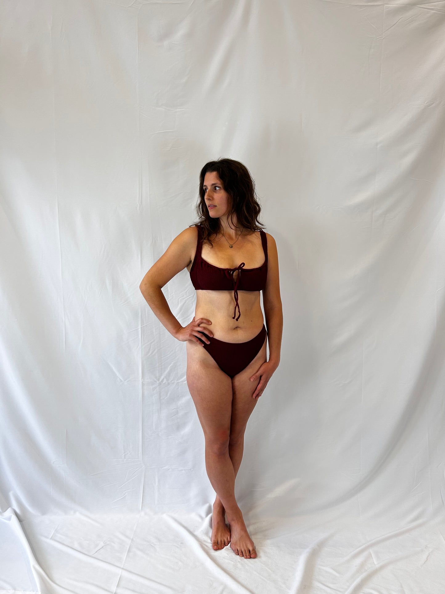 Bikini top is the milkmaid style tie front crinkle fabric. Bikini bottom is the high rise cheeky textured crinkle fabric. Model wears the two piece bikini in burgundy.