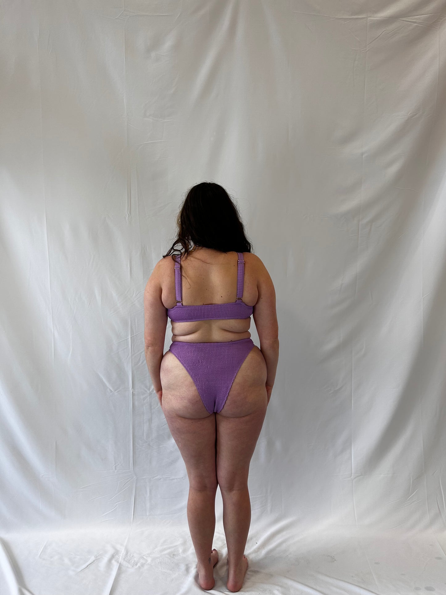 Lavender two piece bikini from the back. Model wears the milkmaid style tie front crinkle fabric bikini top. Bikini bottom is the high rise cheeky textured crinkle fabric.