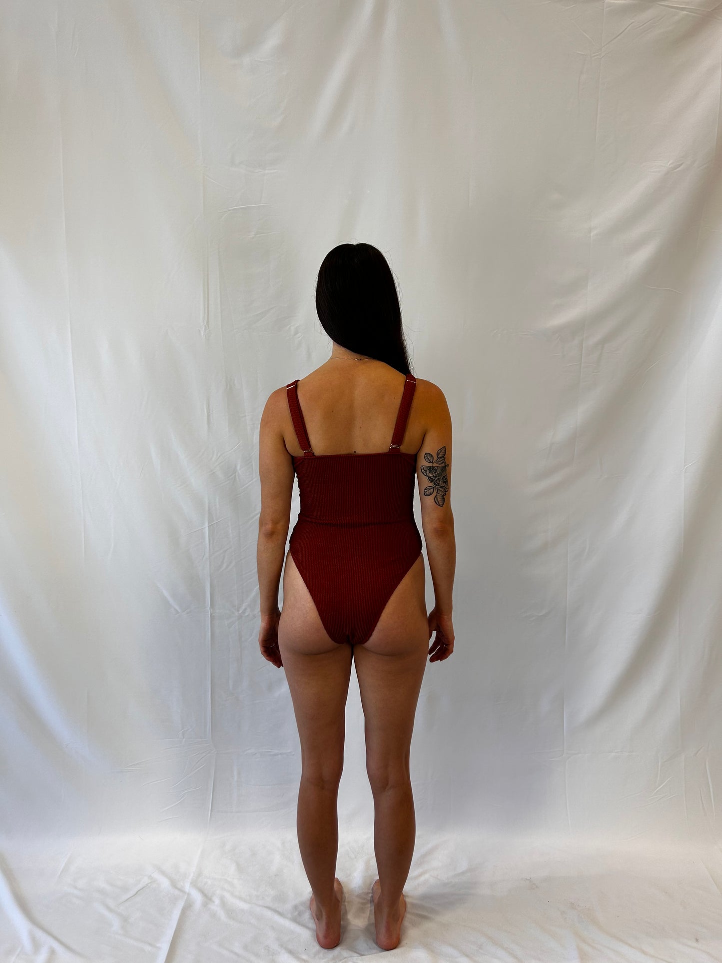 Rust one piece from the back. Woman wears the milkmaid style tie front crinkle fabric one piece. Rust one piece is high cut and cheeky.