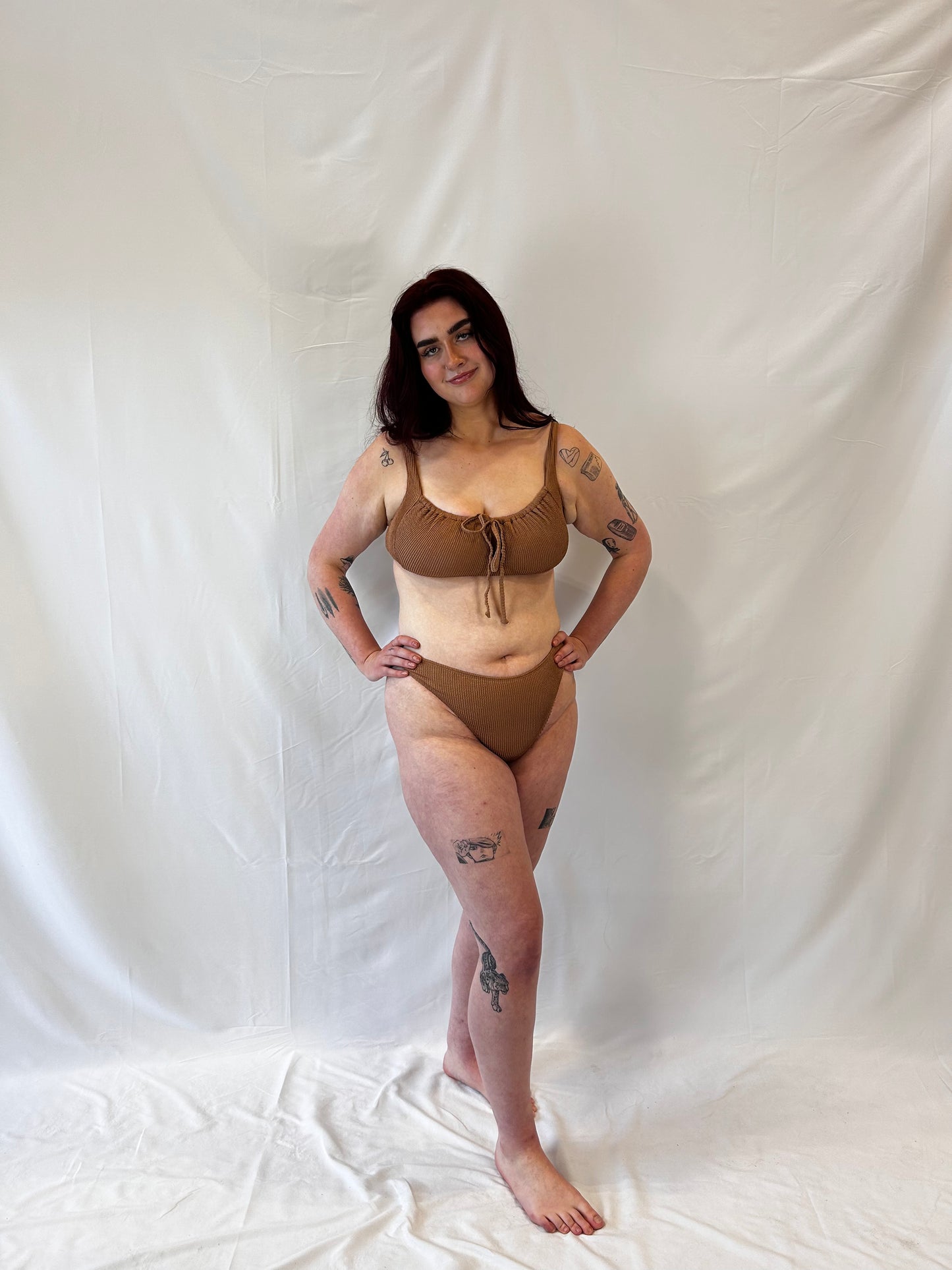 Model wears the milkmaid style tie front crinkle fabric bikini top. Model wears the high rise cheeky textured crinkle fabric bikini bottom in beige.