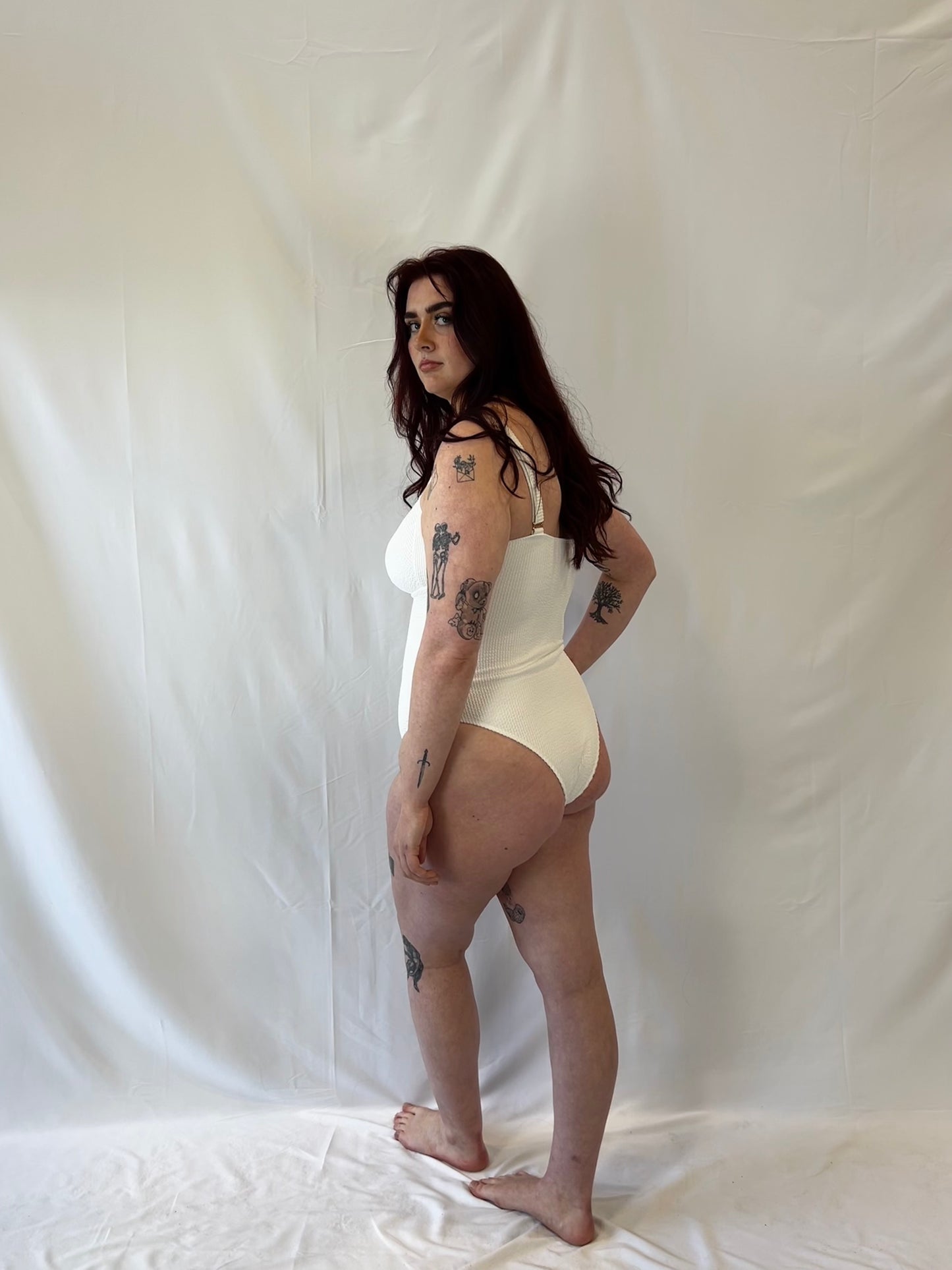 Side view of the white one piece swimsuit. Woman wears the milkmaid style tie front crinkle fabric one piece. White one piece is high cut and cheeky.