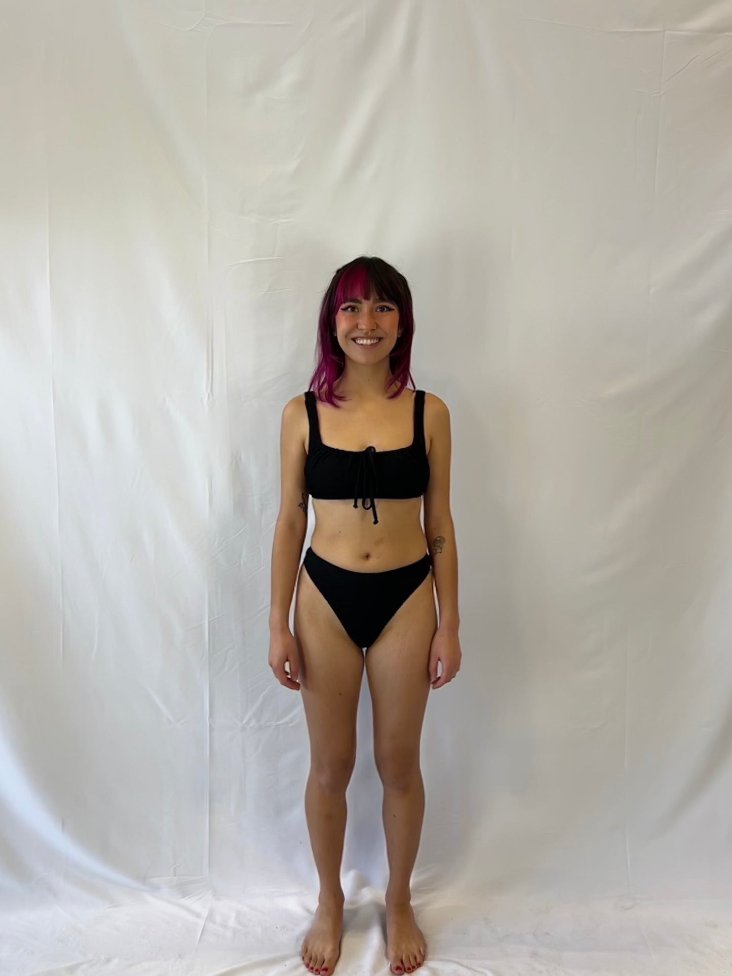 Bikini top is the milkmaid style tie front crinkle fabric. Bikini bottom is the high rise cheeky textured crinkle fabric. Model wears the black two piece bikini.