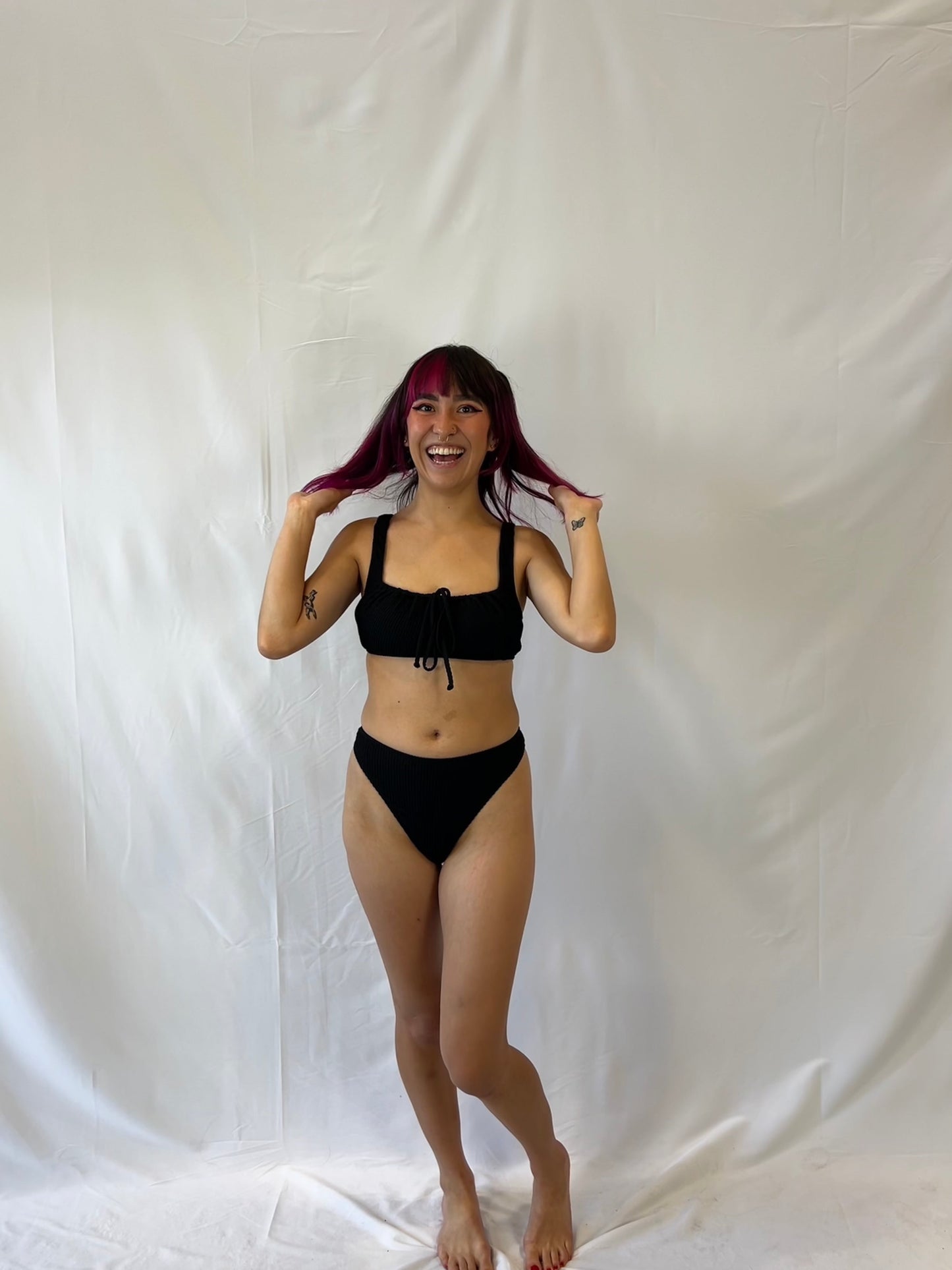 Bikini top is the milkmaid style tie front crinkle fabric. Bikini bottom is the high rise cheeky textured crinkle fabric. Model wears the black two piece bikini.