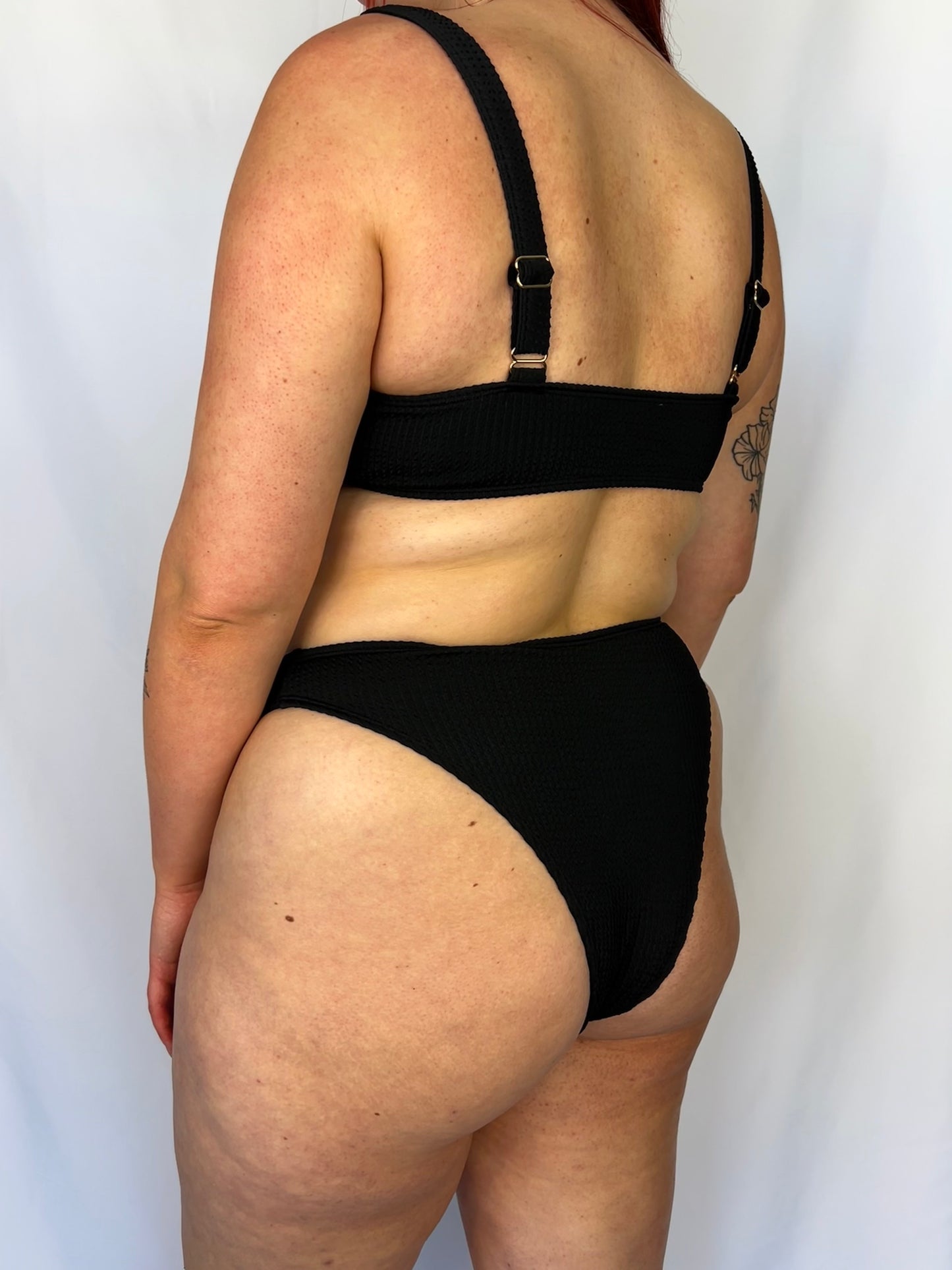 Model wears the high rise cheeky textured crinkle fabric bikini bottom. Close up of the black bikini bottom from the side.