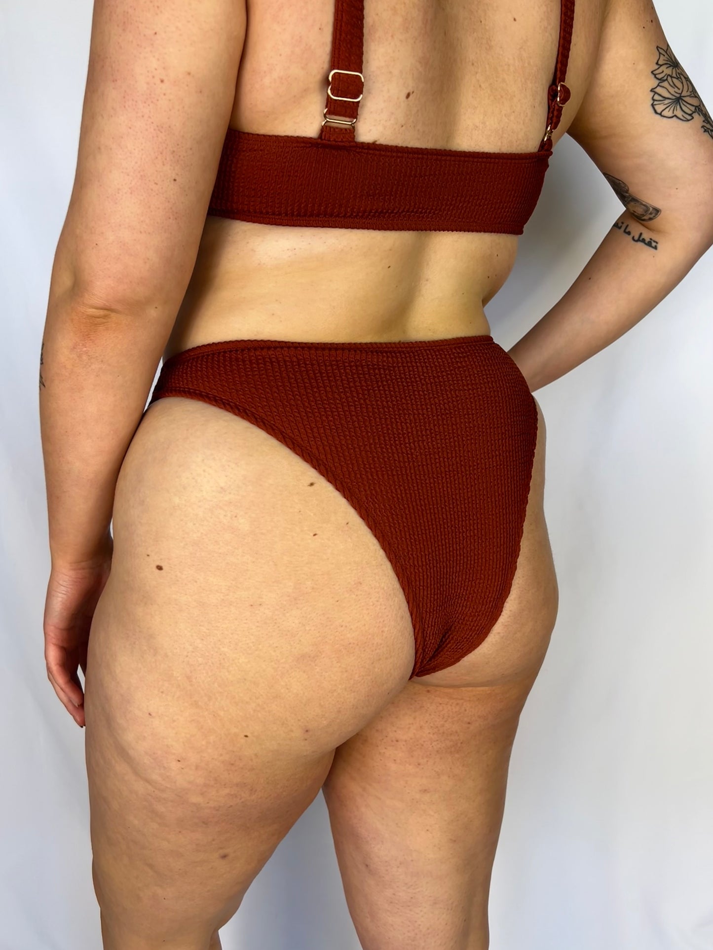 Close up of the rust bikini bottom from the back. Model wears the high rise cheeky textured crinkle fabric bikini bottom.