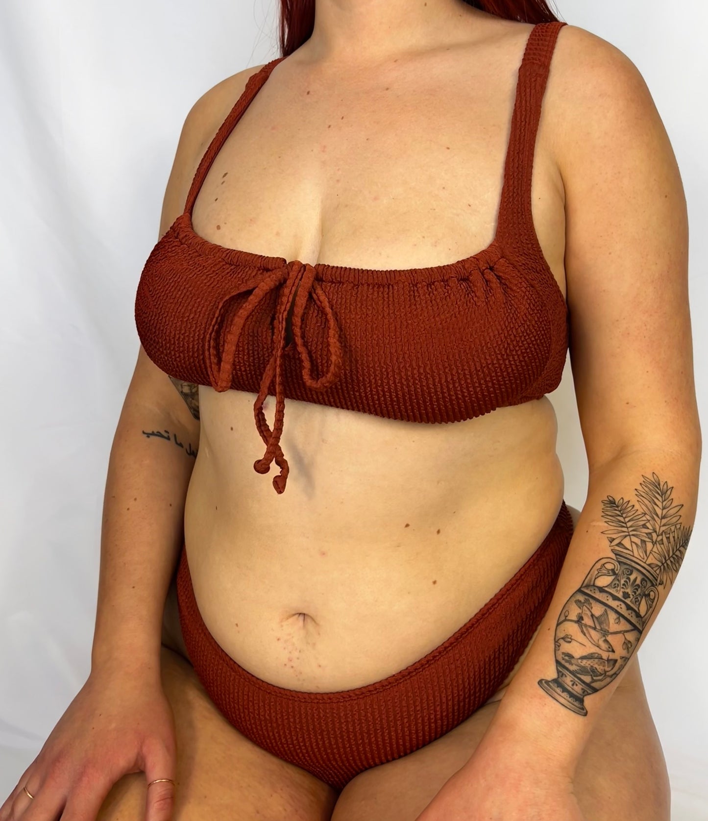 Close up of the two piece bikini top in rust from the front. Bikini top is the milkmaid style tie front crinkle fabric. Bikini bottom is the high rise cheeky textured crinkle fabric.