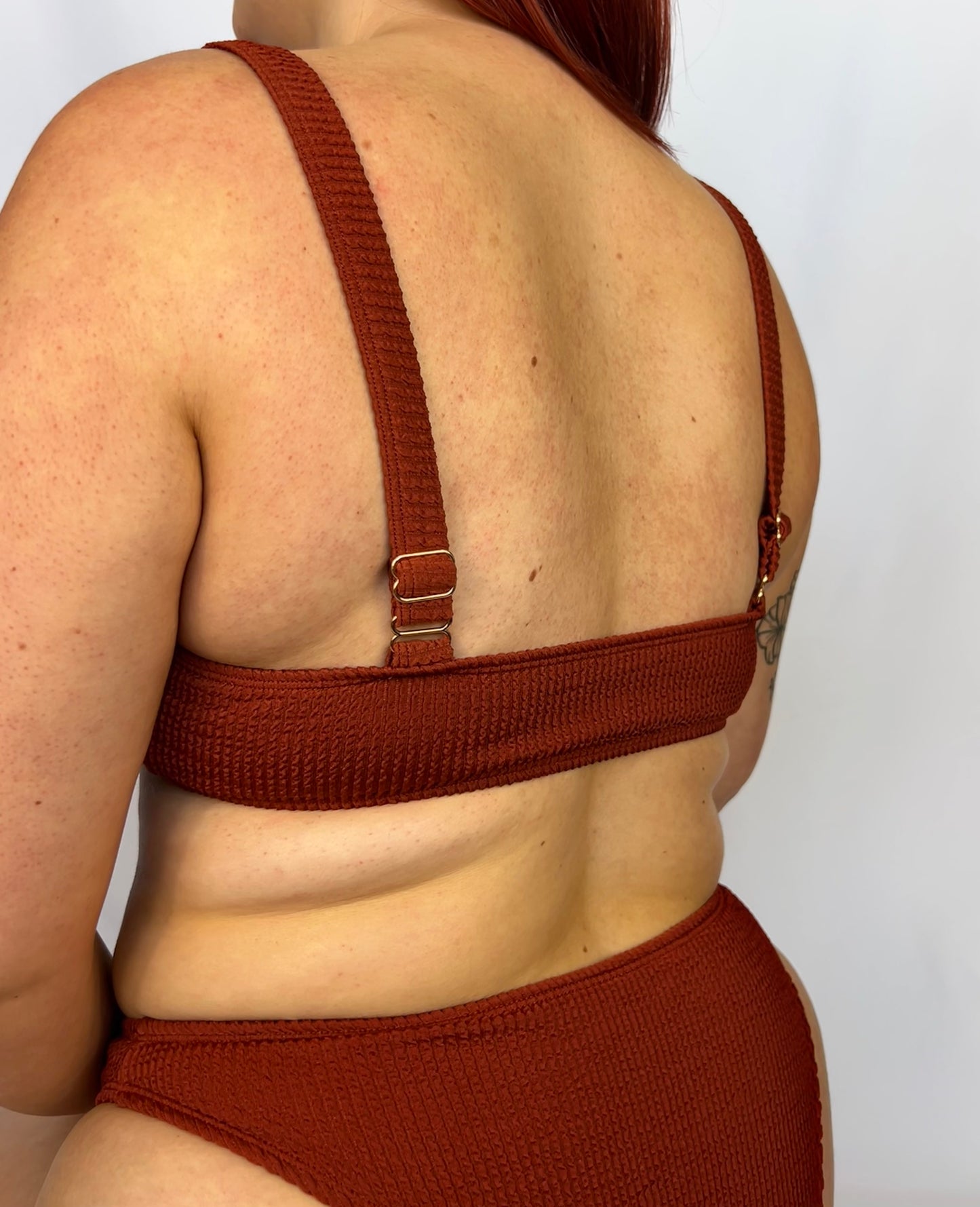 Close up of the two piece bikini top in rust from the back. Rust two piece bikini from the back. Model wears the milkmaid style tie front crinkle fabric bikini top.