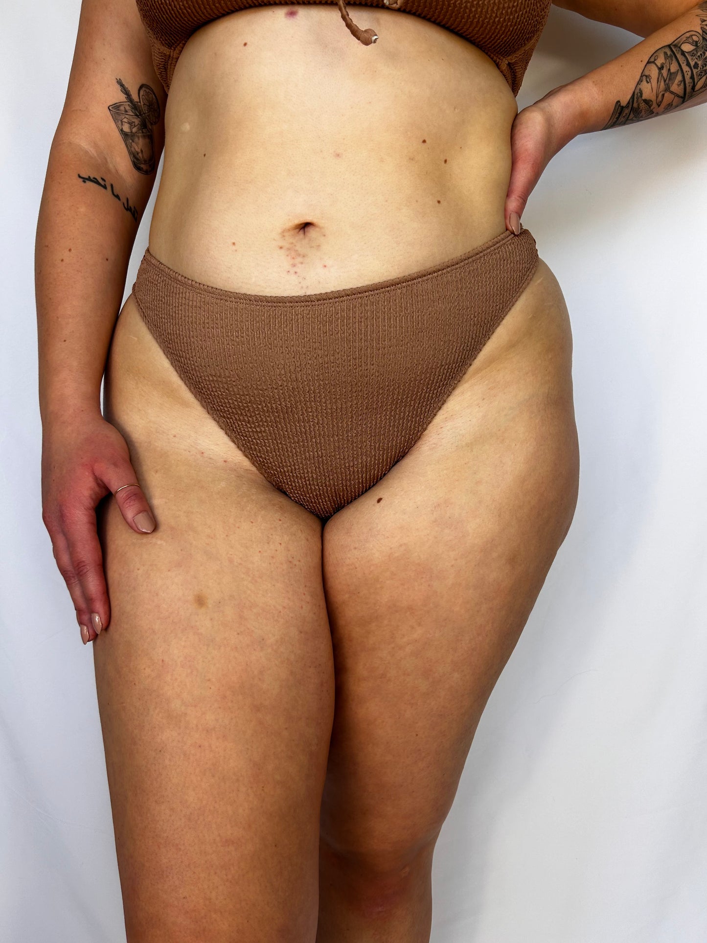 Model wears the high rise bottom. Cheeky bikini bottom with textured crinkle fabric in beige.