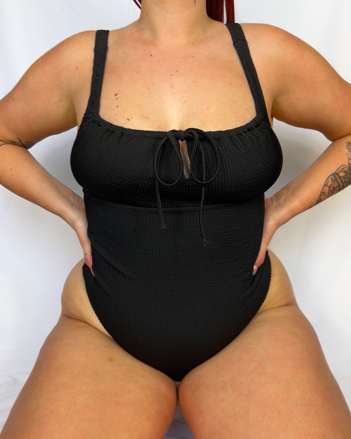 Close up of the black one piece from the front. Swimsuit is the milkmaid style tie front crinkle fabric one piece. Black one piece is high cut and cheeky.