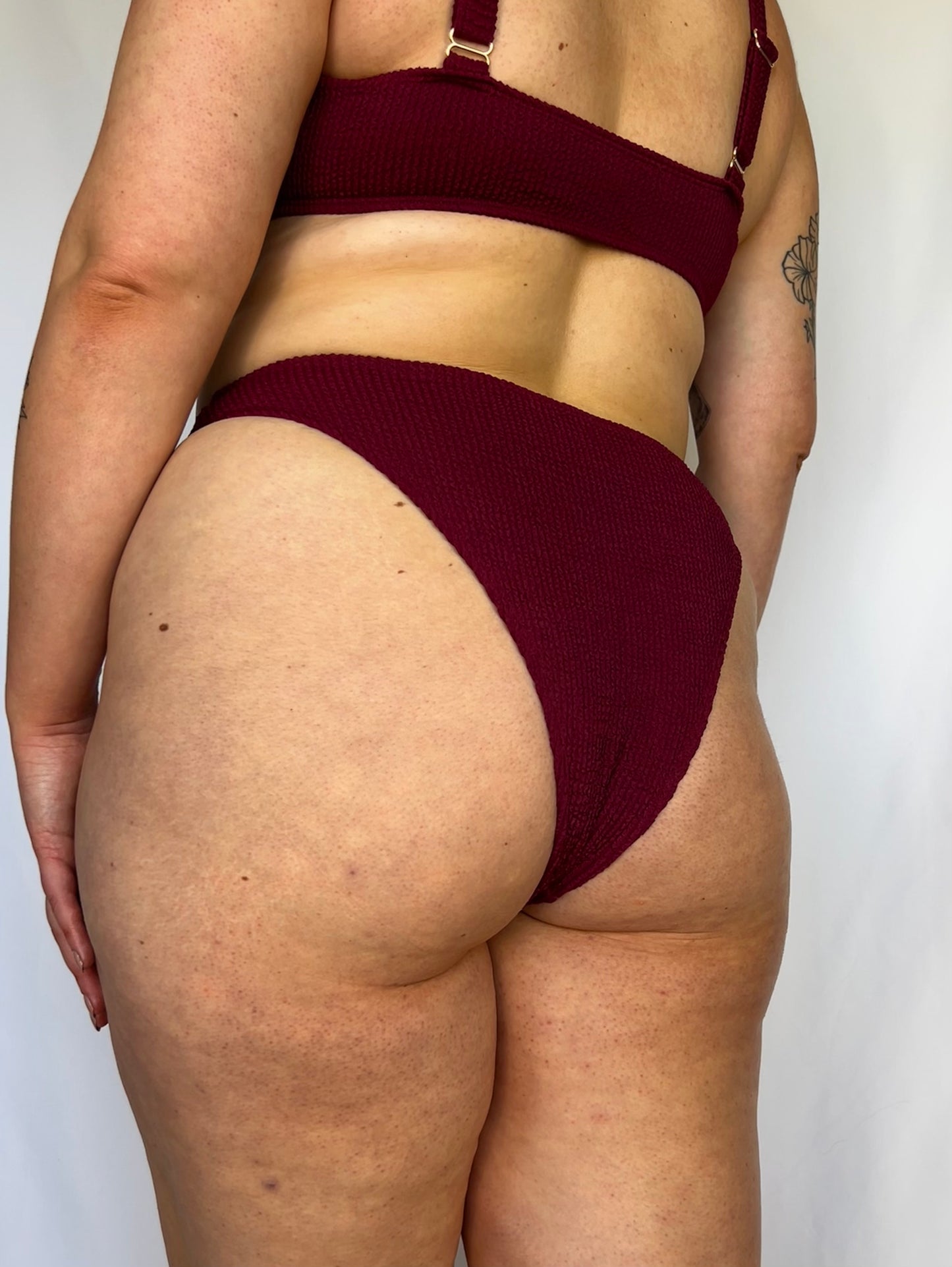 Model wears the high rise cheeky textured crinkle fabric bikini bottom. Burgundy bikini bottom close up from the back.