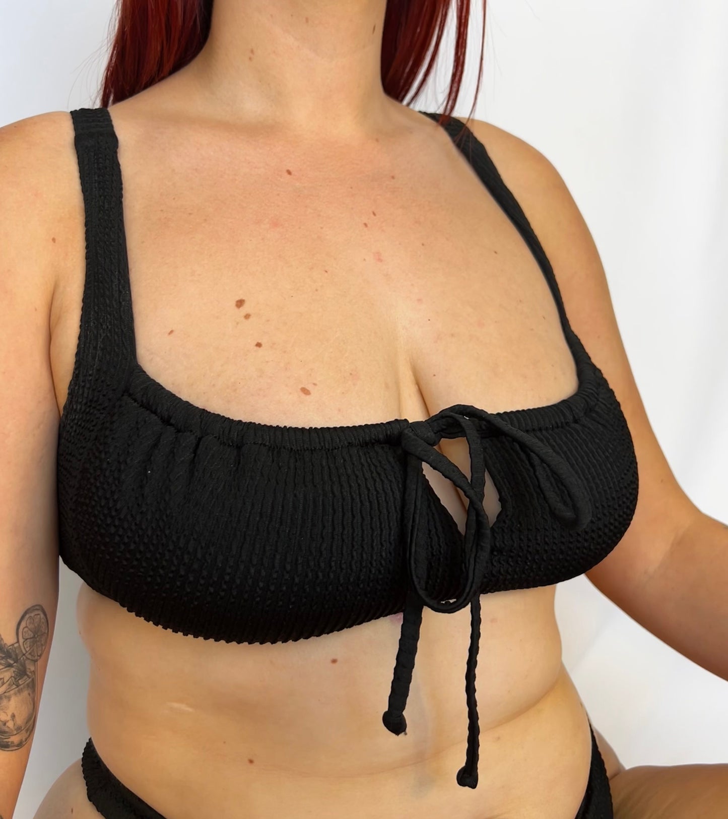 Close up of the two piece bikini top in black from the front. Model wears the milkmaid style tie front crinkle fabric bikini top.