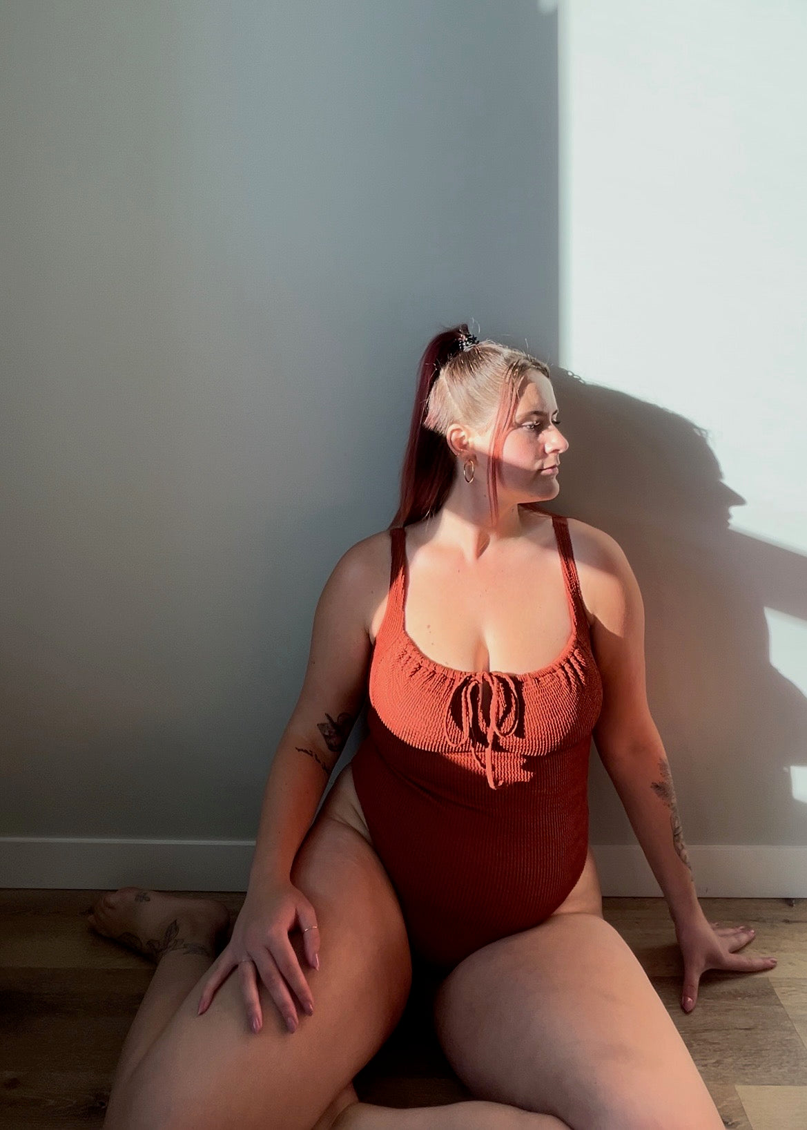 Woman wears the milkmaid style tie front crinkle fabric one piece. Rust one piece is high cut and cheeky.