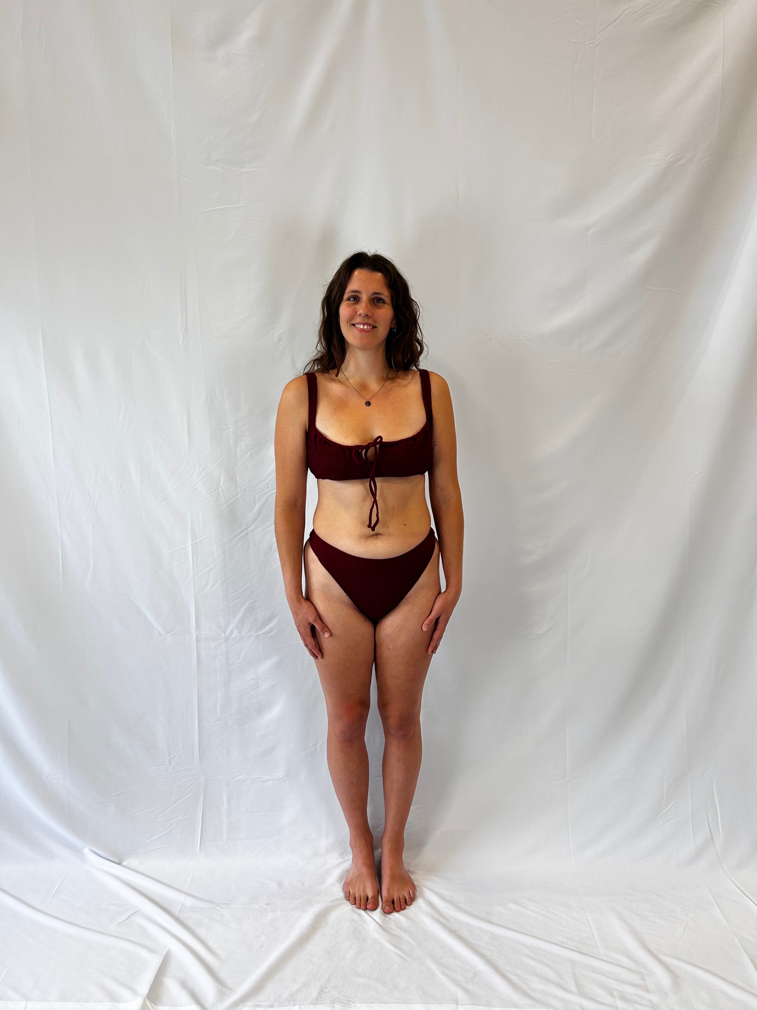 Bikini top is the milkmaid style tie front crinkle fabric. Bikini bottom is the high rise cheeky textured crinkle fabric. Burgundy two piece bikini from the front.