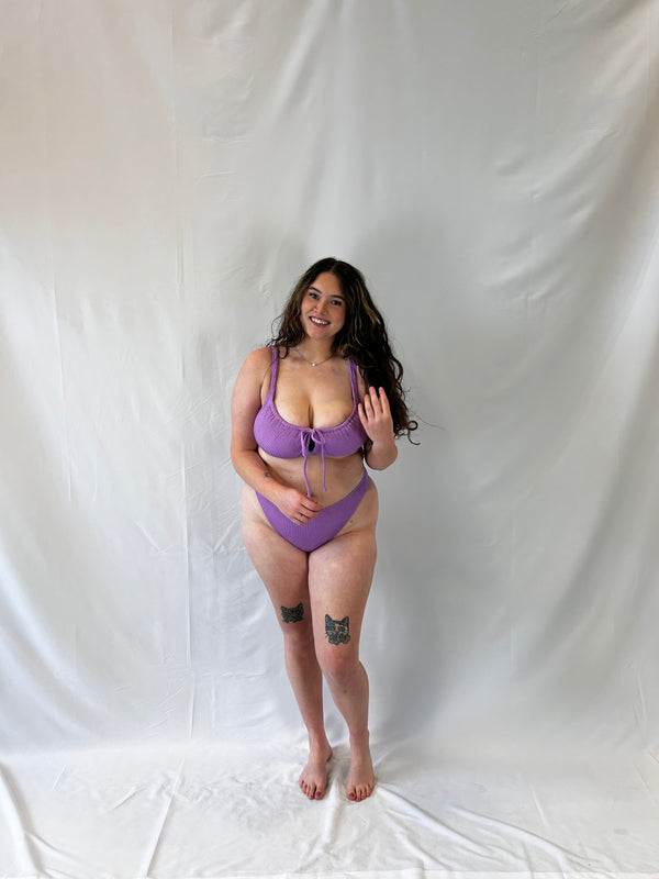 Model wears the lavender two piece bikini. Bikini top is the milkmaid style tie front crinkle fabric. Bikini bottom is the high rise cheeky textured crinkle fabric. 