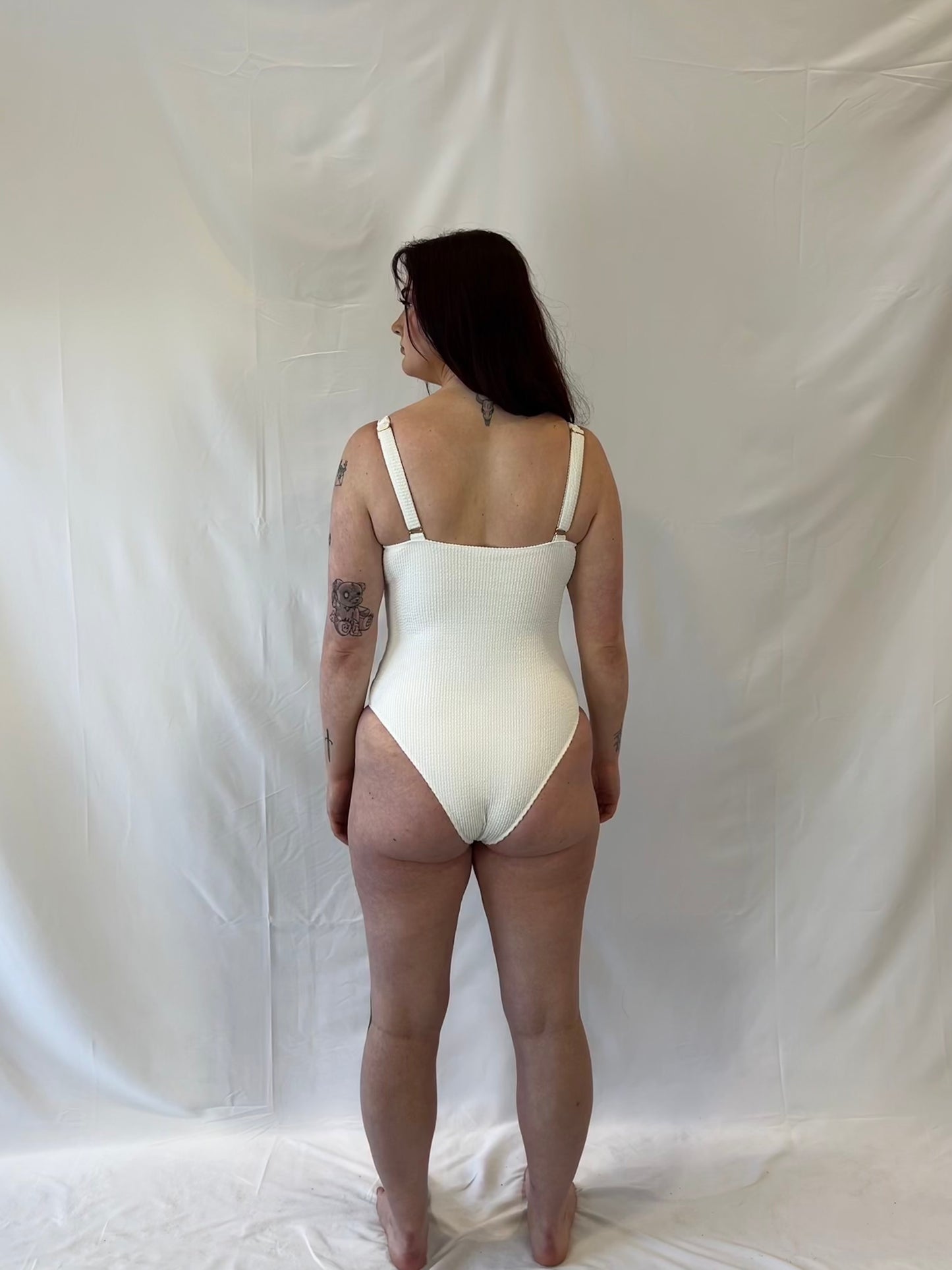 White one piece swimsuit from the back. Woman wears the milkmaid style tie front crinkle fabric one piece. White one piece is high cut and cheeky.  