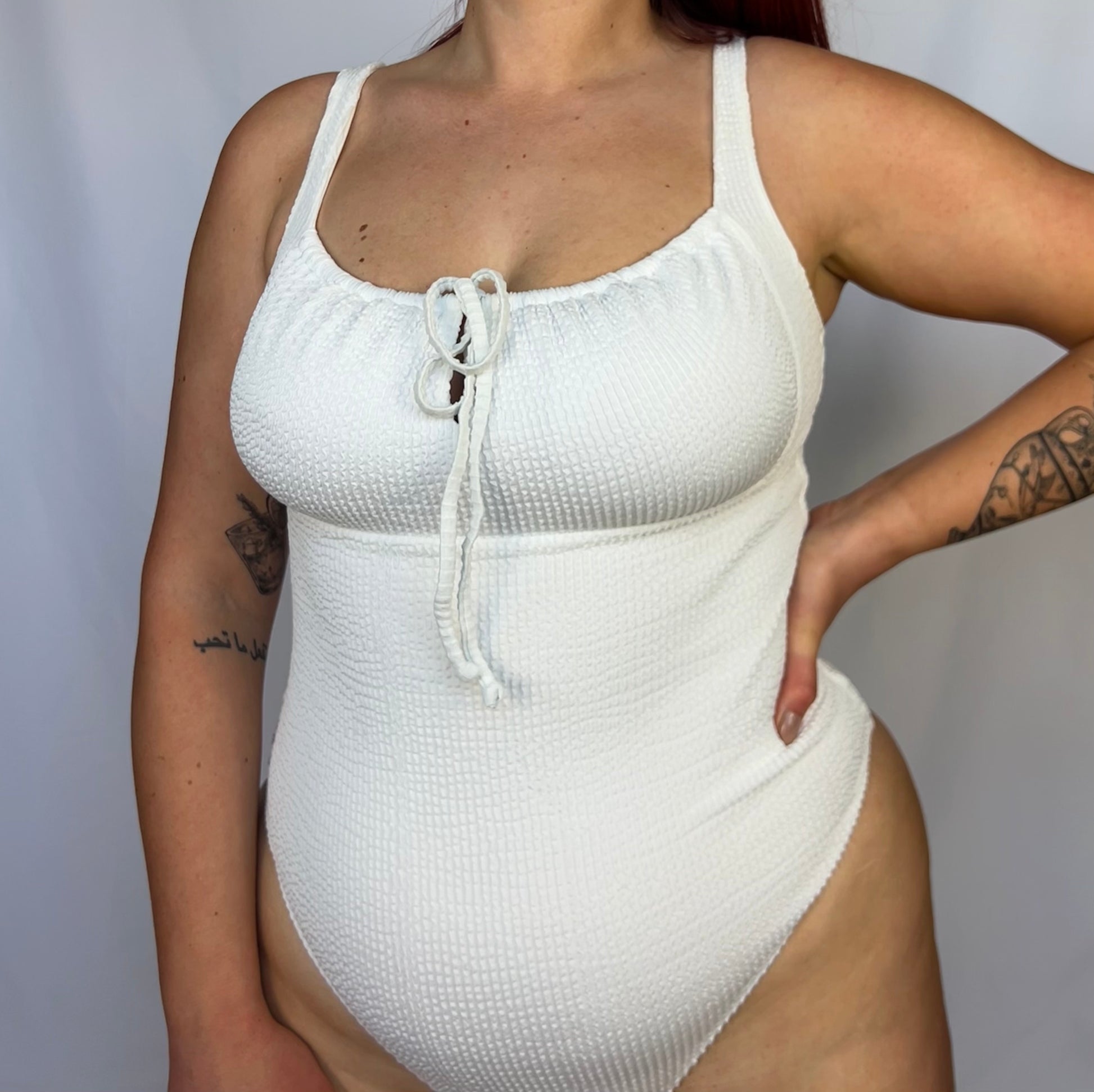 Close up of the white one piece from the front. Swimsuit is the milkmaid style tie front crinkle fabric one piece. White one piece is high cut and cheeky. 