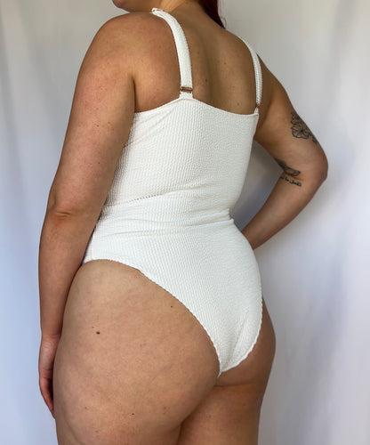Close up of the white one piece swimsuit from the back. Swimsuit is the milkmaid style tie front crinkle fabric one piece. White one piece is high cut and cheeky. 