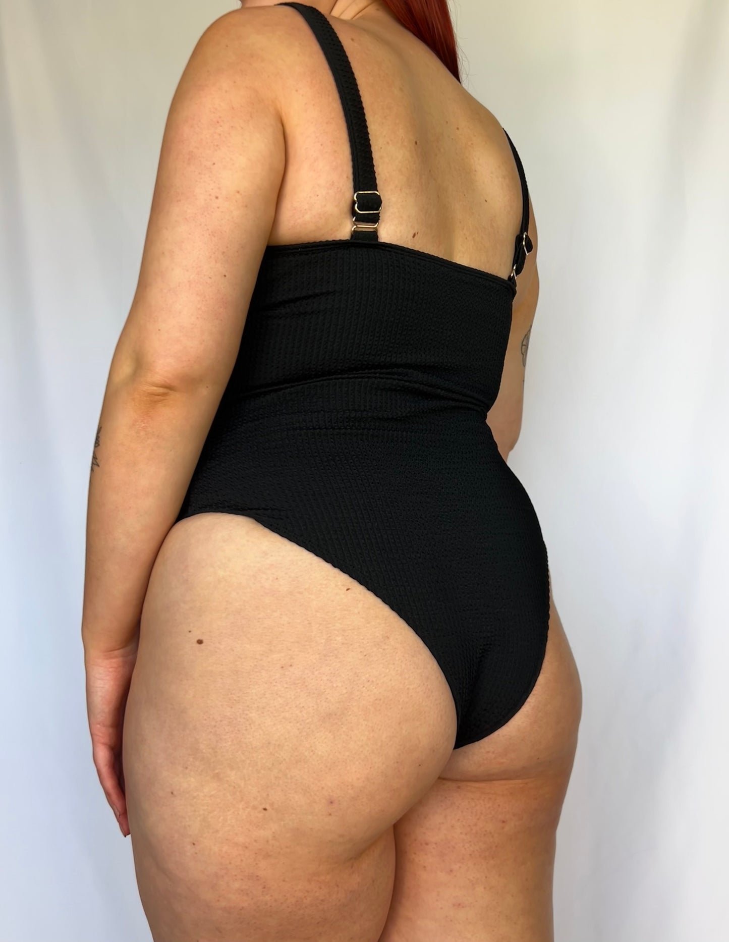 Close up of the black one piece from the back. Swimsuit is the milkmaid style tie front crinkle fabric one piece. Black one piece is high cut and cheeky. 