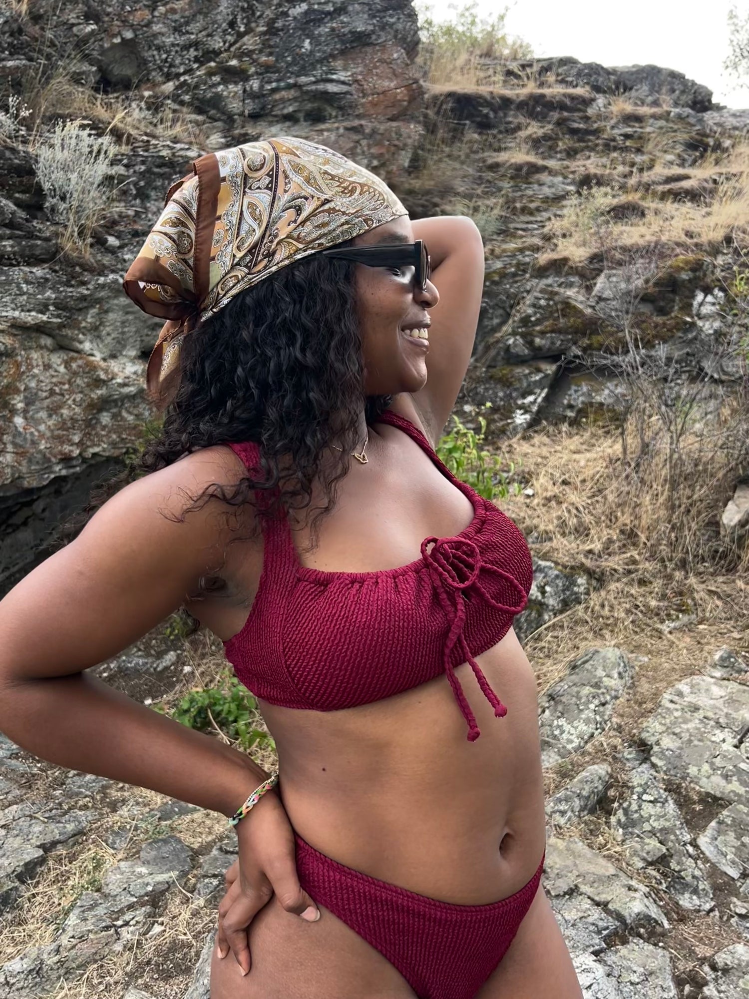 Woman in a burgundy bikini and patterned bandana standing on rocks